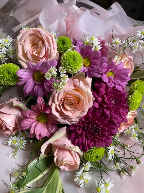 A floral bouquet featuring pale pink roses, vibrant purple daisies, bright green chrysanthemum-like flowers, and small white daisy-like blossoms with yellow centers, all arranged with green foliage an