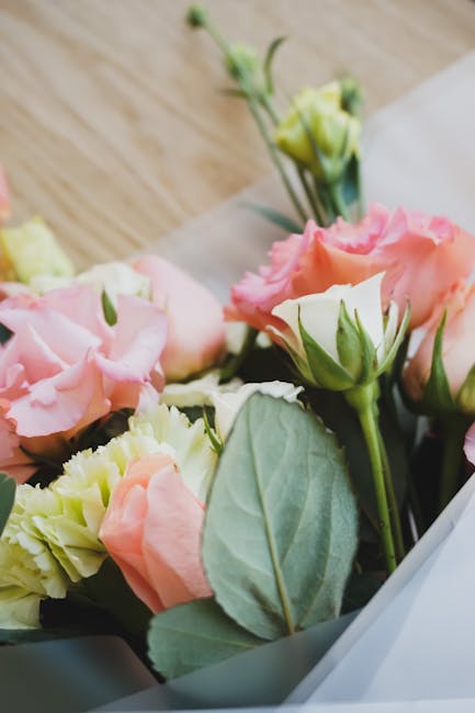 A close-up of a floral bouquet featuring soft pink and cream Lisianthus flowers with delicate, ruffled petals and pale green leaves. The blooms are arranged in a natural, slightly dispersed style, res