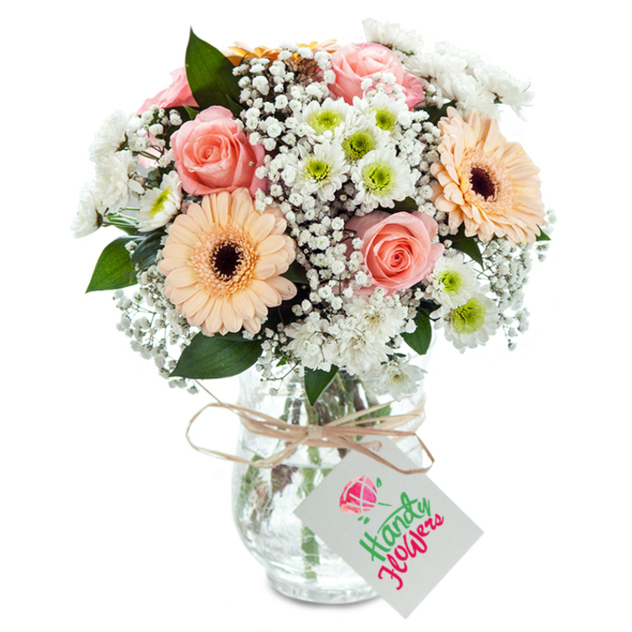 Professionally designed by local florists in Archway, this elegant bouquet serves as a refined tribute to the area's blend of tradition and modernity. Lush, peach-pink roses occupy pride of place-each bloom expertly opened to reveal swirling, velvety petals that embody classic romance. Standing tall beside them, two peach-hued gerbera daisies with striking dark centers introduce a splash of joviality, their symmetry echoing the energetic bustle of Junction Road. Among the major blooms, tufts of airy baby's breath intermingle, forming a delicate white mist that softens the bouquet's structure and bridges the colours. Small white chrysanthemums with distinct lime-green centers are scattered throughout, injecting freshness and a gentle surprise at every angle. Touches of eucalyptus and deep green foliage are thoughtfully woven in, enhancing both aroma and the composition's layered depth. The arrangement resides in a clear, textured glass vase-a nod to the timeless tableware often seen in Archway's historic homes. The ensemble is completed by a slender natural twine bow tied at the neck, allowing a neat white tag to dangle gracefully, perfect for carrying a personal message. The entire presentation is bathed in soft, clean light, illuminating each detail and making the bouquet an ideal centrepiece for celebrations, anniversaries, or simply brightening the everyday in Archway.