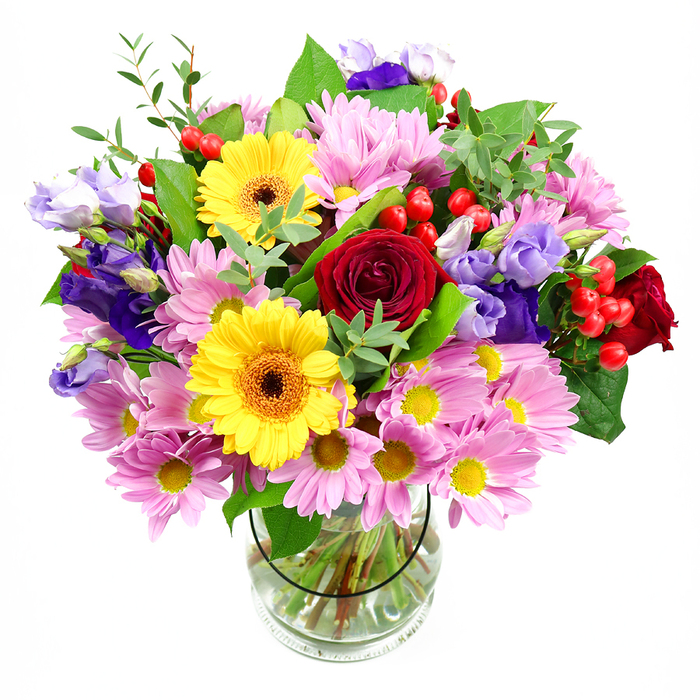 A vibrant mixed-colour bouquet overflows from a simple, clear glass vase, photographed against a crisp white background that makes every shade appear bright and defined. At its core, lush red roses open like velvet spirals, their deep crimson tones bringing a sense of classic romance and heartfelt sincerity. Flanking them are two bold yellow gerbera daisies, lifted on sturdy stems, their wide petals encircling brown-orange centres that introduce a warm, contemporary contrast and add a sense of cheerful personality. Around this central cluster, pink daisies or chrysanthemums spread gently outward, each bloom composed of numerous slender petals around a soft yellow centre, building a cloud of pastel colour that softens and enlarges the silhouette. Interspersed among them, purple and lavender lisianthus sway lightly, their bell-shaped blossoms and buds lending fluid lines and cool-toned elegance, reminiscent of quiet corners of Highgate Wood not far from Archway. Here and there, bright red hypericum berries cluster like tiny orbs, their smooth, glossy skins catching the light and contributing a playful, textural sparkle. Enveloping the entire arrangement is an assortment of foliage in layered greens, from sturdy, darker leaves that provide depth to lighter, airy sprigs that suggest movement and the feel of freshly gathered garden stems. The clear glass vase reveals straight, carefully trimmed stems standing in clear water, offering a glimpse of the structure supporting the lush top. The overall mood is upbeat and welcoming, ideal for setting on a dining table in an Archway flat, bringing colour into a home office off Junction Road, or arriving as a same-day floral gift that carries local charm and the crafted precision of an experienced neighbourhood florist.