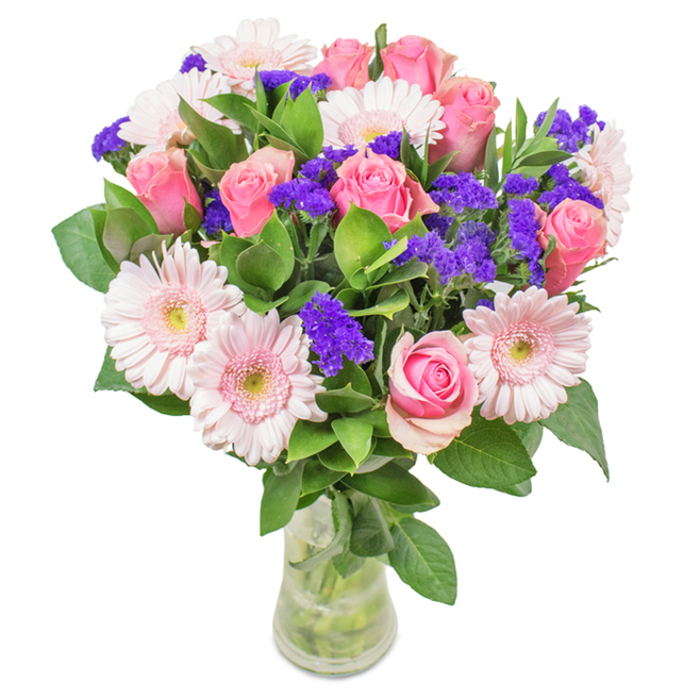This vibrant bouquet, elegantly displayed in a clear glass vase, features approximately seven to nine pink roses-some with petals just starting to unfurl, others opening into classic spirals-alongside five to seven delicate pale pink gerbera daisies with large, rounded heads and creamy centers. Sprays of bright purple statice weave between the blooms, lending visual texture and depth that echoes the creative vibrancy of Archway's local scene. The lush green foliage provides a full, verdant base, reminiscent of the leafy expanses found in Waterlow Park. The transparent vase reveals the criss-crossed stems and fresh water below, reinforcing the sense of newly gathered beauty. Ideal for birthdays, anniversaries, Mother's Day, or as a charming decorative highlight, this arrangement combines pink roses, gerberas, and statice with the refined eye of an Archway florist-exuding joy, celebration, and heartfelt affection, ready for delivery across N19 and beyond.